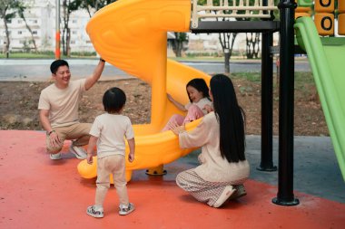 Gülümseyen ebeveynler ve iki küçük çocuk renkli bir oyun alanında oyun zamanının tadını çıkarıyorlar..