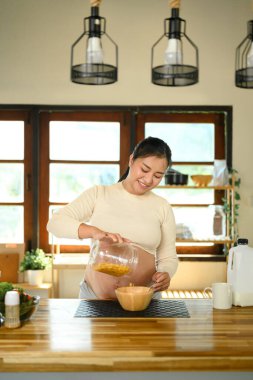 Asyalı hamile kadın aydınlık bir mutfakta hafif bir yemek hazırlıyor..