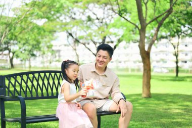 Baba ve kızı güneşli bir günde parktaki bankta oyuncağın tadını çıkarıyorlar..