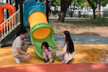 Gülümseyen ebeveynler ve iki küçük çocuk renkli bir oyun alanında oyun zamanının tadını çıkarıyorlar..