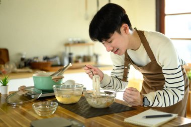 Mutfak tezgahında yeni pişmiş erişte yiyen gülümseyen genç adam..