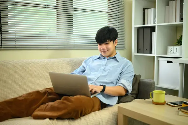 Genç adam evdeki bilgisayarını ya da internet eğlencesini kullanarak kanepede dinleniyor..