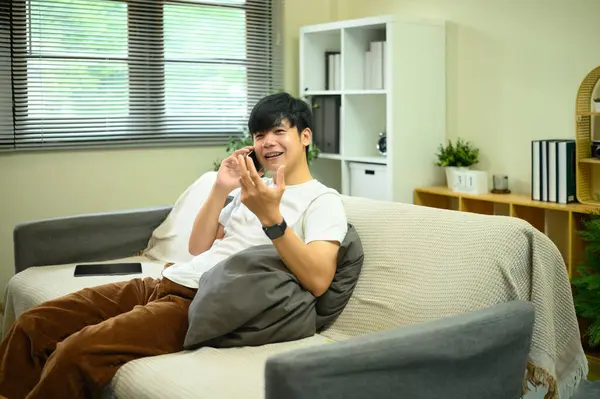 Evdeki kanepede oturan genç bir adam, rahat bir oturma odasında telefon görüşmesi yapıyor..