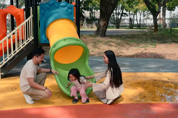 Gülümseyen ebeveynler ve iki küçük çocuk renkli bir oyun alanında oyun zamanının tadını çıkarıyorlar..