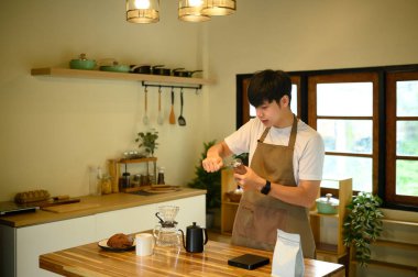 Önlüklü genç adam ev mutfağında taze kahve çekirdeklerini öğütüyor..