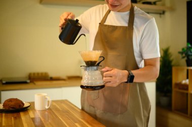 Önlük giymiş bir adam sıcak bir mutfakta kahvenin üzerine kahve döker..