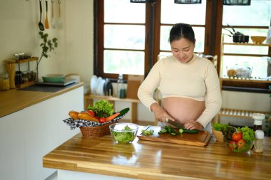 Hamile kadın parlak bir mutfakta sağlıklı bir salata hazırlıyor..