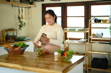Hamile kadın parlak bir mutfakta sağlıklı bir salata hazırlıyor..