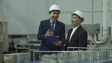 Kasklı fabrika yöneticileri üretim tesisinde metal kutularla taşıma bandını inceliyor..