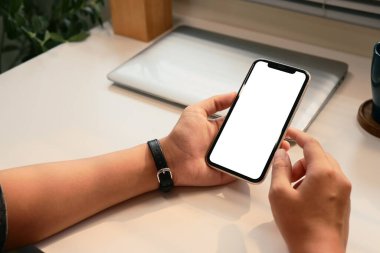 Ofis masasında boş beyaz bir ekranla akıllı telefonu tutan elleri kapatın..