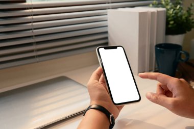 Temiz beyaz bir masanın üzerinde boş bir ekranla akıllı telefonu tutan eller..