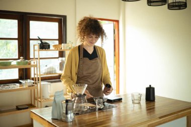 Gülümseyen kadın, güneş ışığıyla aydınlatılmış mutfakta kahve hazırlıyor..