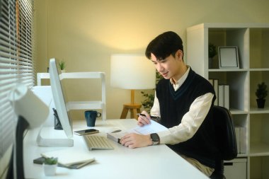 Beyaz bir masada otururken bir belge üzerinde çalışan odaklanmış Asyalı erkek..