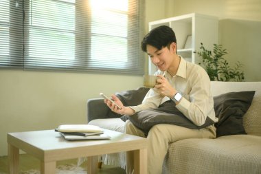 Gülümseyen erkek elinde bir bardak ve akıllı telefonundaki mesajları kontrol ediyor..