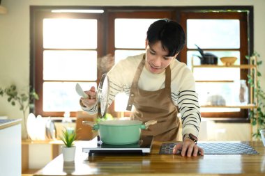 Güneşli, modern bir mutfakta yemek hazırlayan önlüklü, gülümseyen adam..