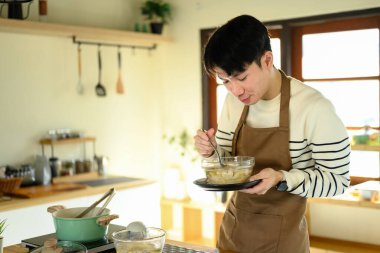 Önlüklü genç adam sıcak bir mutfakta yeni hazırlanmış bir yemeği tadıyor..