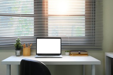 Güneş ışığı panjurların arasından, dizüstü bilgisayar ve dekorla dolu bir masanın üzerine parlıyor..