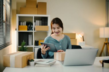 Çevrimiçi mağaza sahibi bilgisayarla çalışma alanında otururken dijital tablet siparişlerini kontrol ediyor.