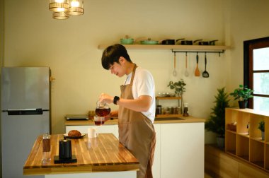 Adam sıcak ışıklandırmalı, taze demlenmiş kahveyi mutfaktaki fincana dolduruyor..