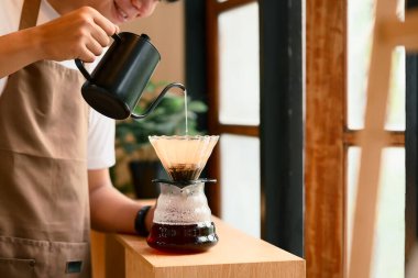 Önlüklü genç adam sıcak mutfakta kahve hazırlıyor..