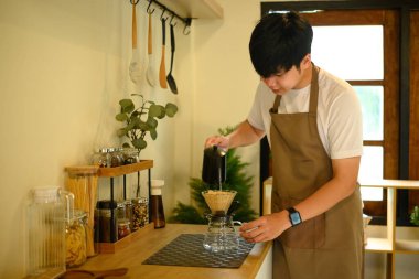 Asyalı bir adam modern, düzenli bir mutfakta taze kahve hazırlıyor..