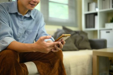 Kanepede oturan akıllı telefon kullanan genç adama yakın çekim.