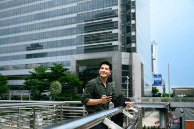 Gülümseyen işadamı bir iş bölgesinde korkuluk başında telefonu tutuyor..