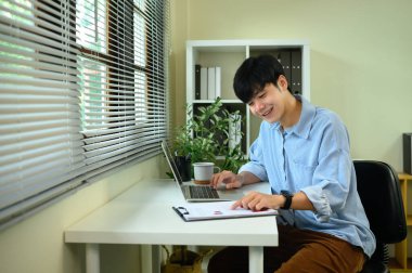 Modern bir masada çalışırken dijital tablet kullanan gülümseyen Asyalı girişimci.