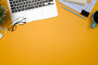 Dizüstü bilgisayarı, kahve fincanı ve parlak sarı arka planda aksesuarları olan yaratıcı masa...