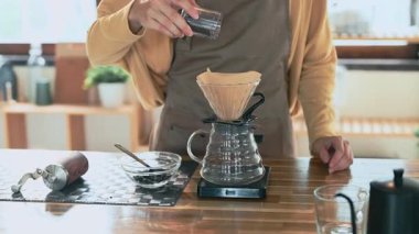 Önlük giymiş odaklanmış bir kadın evdeki filtre konisine taze kahve döker..