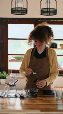 Kahve çekirdeklerini öğütücüye döken genç bir kadın.