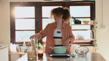 Kıvırcık saçlı genç bir kadın modern ev mutfağında spagetti hazırlıyor..