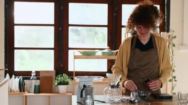 Önlüklü genç bir kadın ev mutfağında demlenmek için kahve çekirdeği topluyor.