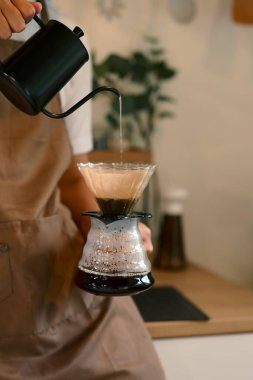 Önlük giymiş bir adam sıcak bir mutfakta kahve üzerine taze kahve hazırlıyor..