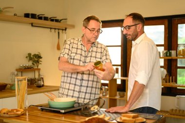 Mutlu kıdemli adam ve yetişkin oğlu parlak bir mutfakta makarna yemeği hazırlıyor. Babalar Günü konsepti.