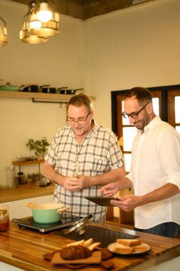 Neşeli baba ve yetişkin oğul birlikte yemek hazırlarken dijital tablette tarifi takip ederler. Babalar Günü konsepti.