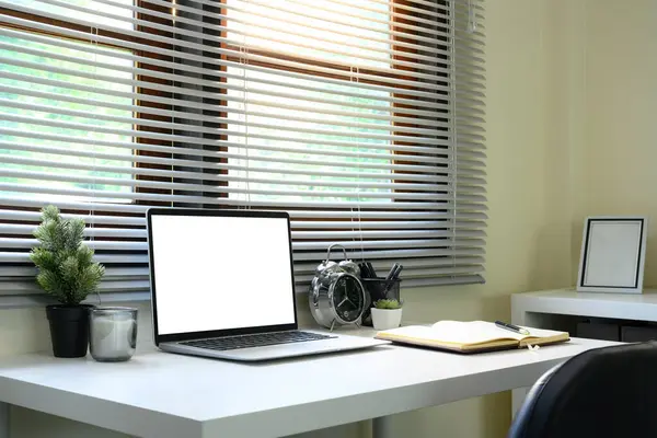 Pencere kenarına dizüstü bilgisayar, defter ve çalar saat kurulumu.