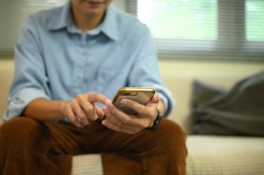 Rahat bir oturma odasında otururken akıllı telefon kullanan gülümseyen adam..