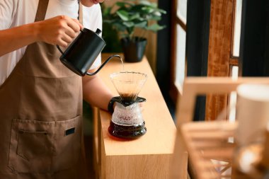 Kahvenin üzerine taze su dökmek için kahve damlatıcısına sıcak su döken adam..