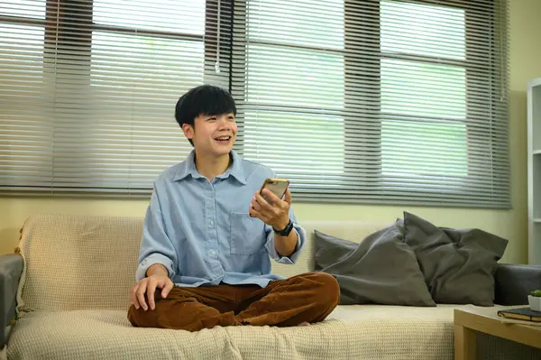 Evdeki kanepede oturan gülümseyen genç adam, elinde akıllı bir telefonla sohbet ediyor..