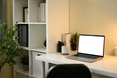 Boş dizüstü bilgisayar, kahve fincanı ve organize raf ile minimalist ev ofisi kurulumu.