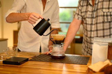 Kıdemli adam ve yetişkin oğlu ahşap mutfak tezgahında el yapımı kahve hazırlıyorlar. Babalar Günü konsepti.