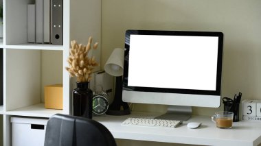 Boş monitör ekranı, vazoda kurumuş çiçekler ve kahve fincanı olan şık bir ofis sahnesi..