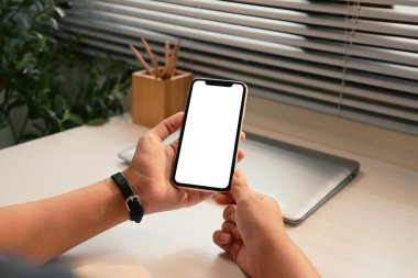 Modern bir çalışma alanında boş ekranlı akıllı telefonu tutan elleri kapatın.