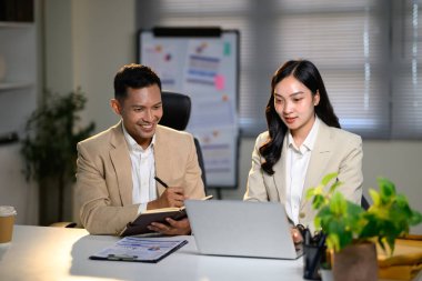 Bir işbirliği sırasında çizelge ve raporları inceleyen gülümseyen meslektaşlar ekibi.