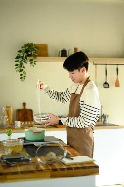 Önlüklü gülümseyen adam sıcak bir evde erişte hazırlıyor..