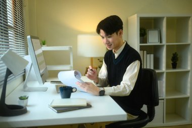 Evrakları inceleyen genç adam yakınlarda bilgisayar ve kahve var..