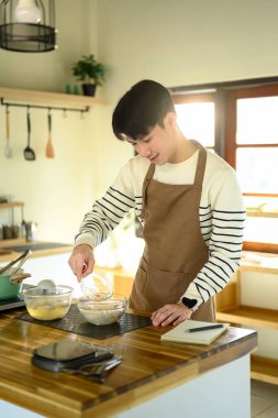 Önlüklü genç adam ocakta yemek hazırlıyor, mutfakta eğleniyor..