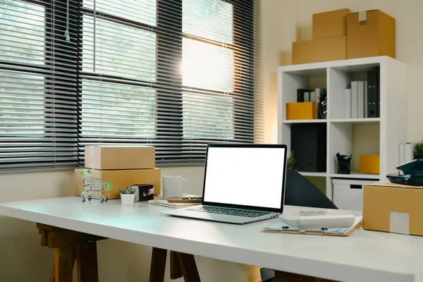 Bilgisayarı, nakliye paketleri ve ambalaj aletleri beyaz bir masanın üzerinde olan e-ticaret merkezi ofisi..