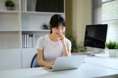 Oturma odasında dizüstü bilgisayar kullanan genç bir kadın..